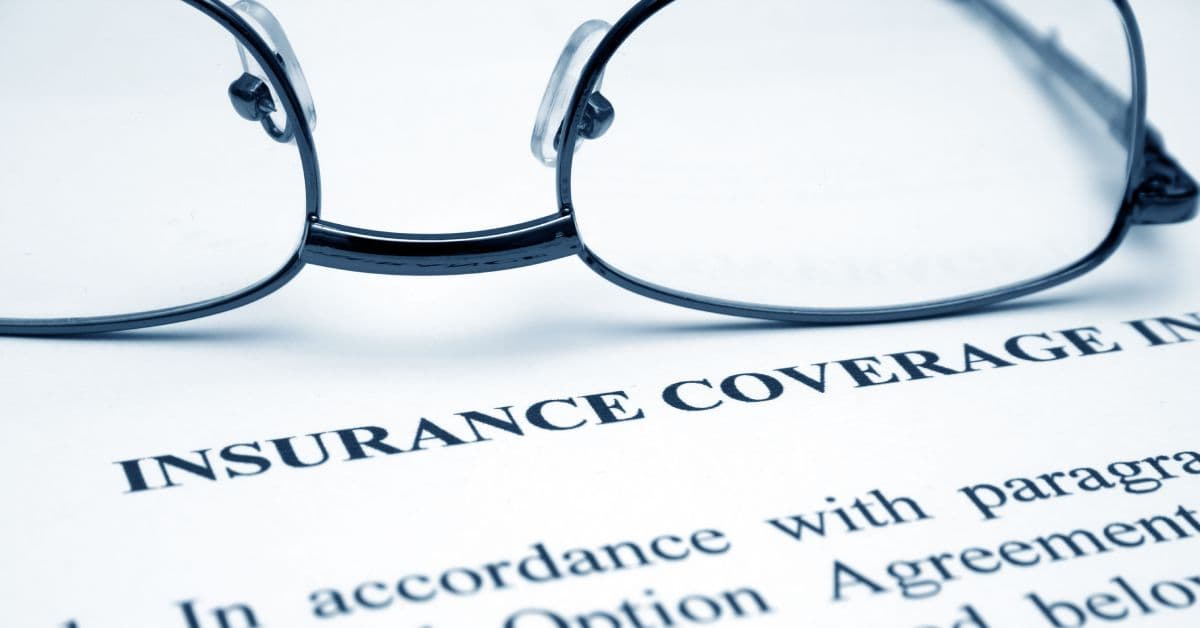 A close-up of a pair of glasses sitting on a white document that says “Insurance Coverage” on the front