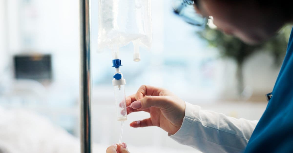 A licensed professional adjusting the IV drip settings on the drip setup. The treatment is setup in someone's home.