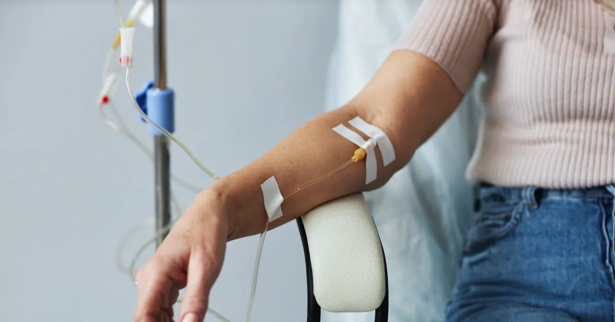 A close-up of a person at home comfortable in a chair as they receive IV therapy through their vein.