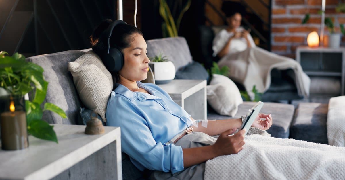 An office space with two employees sit in comfortable chairs to receive IV therapy treatments. One person wears a headset.